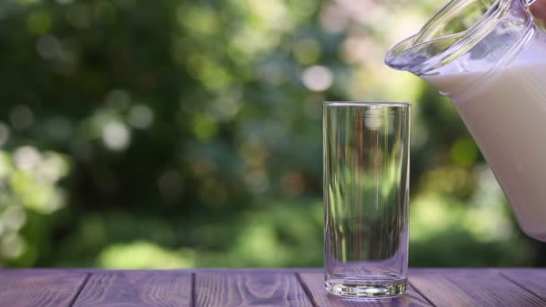 Milk pouring from jug into glass outdoors — Stock Video