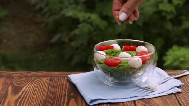 Mano femenina rociando especias en tazón de vidrio con ensalada fresca — Vídeo de stock