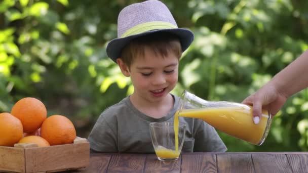 Matka nalévání čerstvé pomerančové šťávy ve sklenici pro syna — Stock video