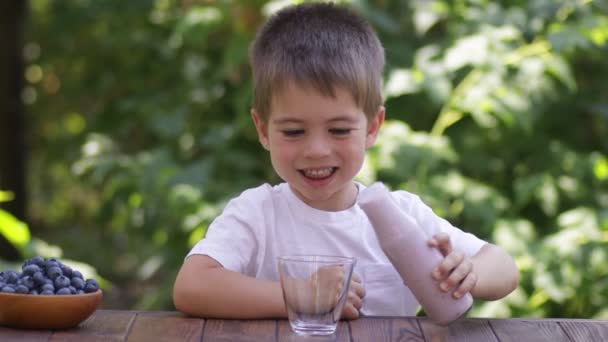 Menino feliz derramando iogurte de mirtilo em vidro — Vídeo de Stock