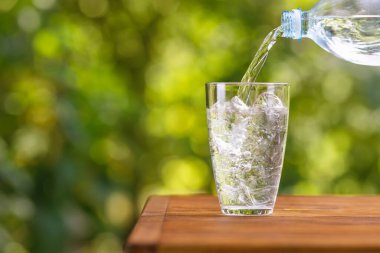 Plastik şişeden akan su, buz küpleriyle dolu cama dökülüyor.