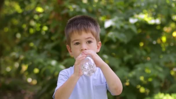 Niño bebiendo agua de la botella de plástico al aire libre — Vídeo de stock