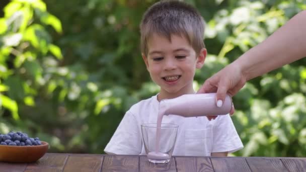 Matka nalévá borůvkový jogurt ve sklenici pro syna — Stock video