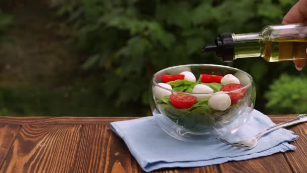 Olijfolie die uit de fles wordt gegoten in een glazen kom met verse salade — Stockvideo