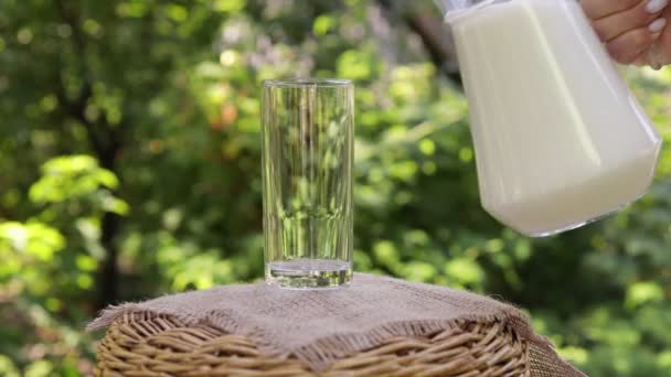 Молоко наливается из кувшина в стекло на открытом воздухе — стоковое видео