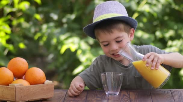 Malý nezávislý chlapec nalévání čerstvé pomerančové šťávy do skla — Stock video