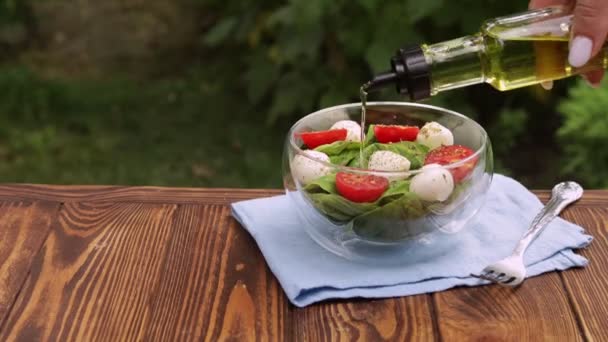 Minyak zaitun dituangkan dari botol dalam mangkuk kaca dengan salad segar — Stok Video