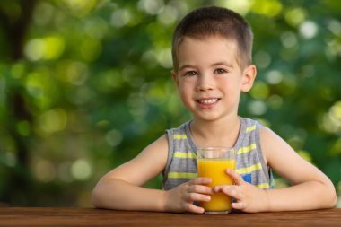 Küçük çocuk dışarıda bir bardak portakal suyu tutuyor.