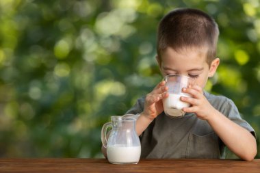 Küçük çocuk dışarıda camdan süt içiyor.