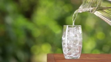 Sürahiden buzla dolu bardağa su dökerek.
