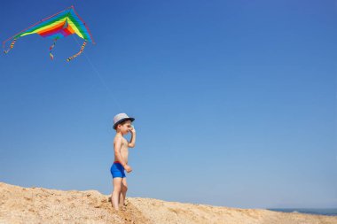 Sahilde renkli uçurtmalı küçük bir çocuk.