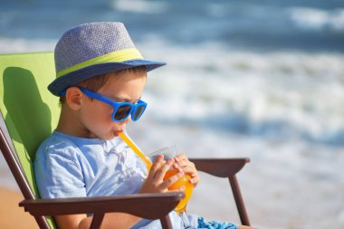 Küçük çocuk deniz kıyısında meyve suyu içiyor.