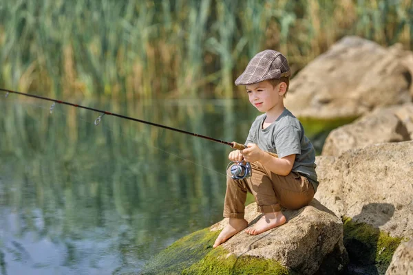 Niño sentado en la piedra y la pesca — Foto de Stock