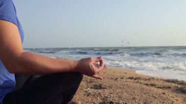 Genç bir kadın deniz sahilinde meditasyon yapıyor.