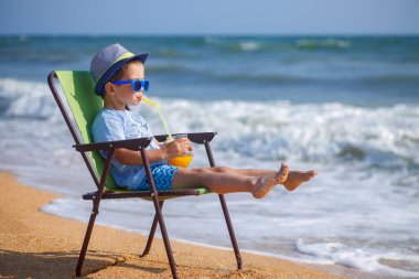 Küçük çocuk deniz kıyısında meyve suyu içiyor.