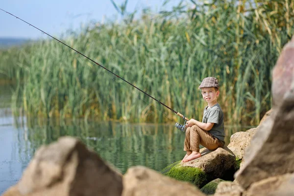 Little boy sitting on stone and fishing — Stock Photo, Image