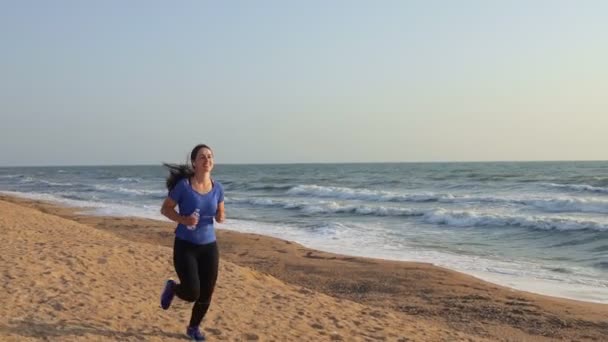 Femeie alergând pe plaja mării și ascultând muzică — Videoclip de stoc