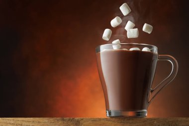 Marşmelovlar kahverengi arka planda sıcak çikolata bardağına dökülüyor..