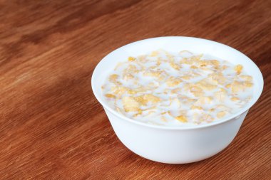 süt ve ahşap bir masa üzerinde beyaz bir kase mısır gevreği