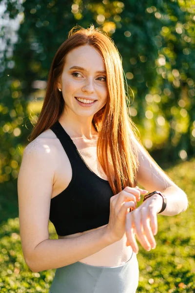 Close-up view of young smiling redhead woman touch on the screen of the smart watch on wrist