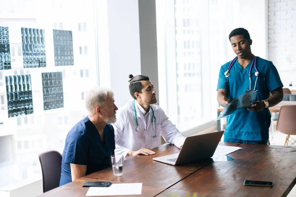 Team of multi-ethnic medical specialists discussing at chest X-ray image during medical conference.