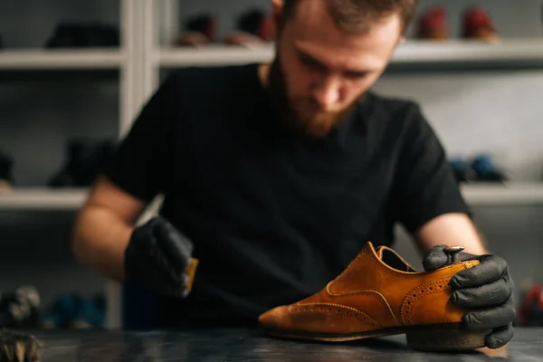 Front view of shoemaker wearing black latex gloves polishing old light brown leather shoes for later restoration.