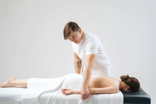 Side view of male masseur massaging hand of female lying on massage table at spa salon.