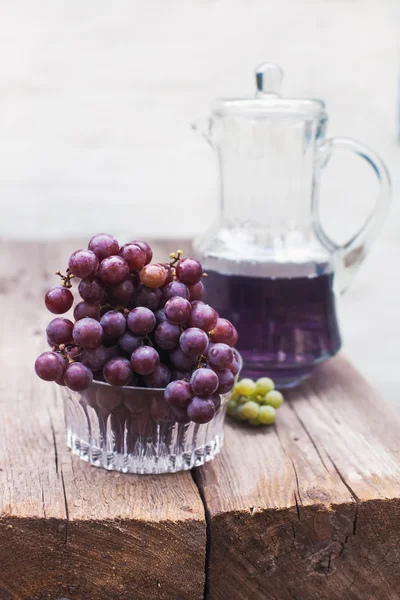 Uvas azuis verdes frescas e garrafa de suco de uva na mesa de madeira — Fotografia de Stock