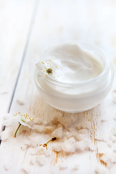 Maceta de crema de belleza rodeada de flores y sal marina sobre una mesa de madera blanca — Foto de Stock