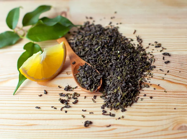 Rodaja de limón y cuchara de hojas de té verde seco sobre fondo de madera — Foto de Stock