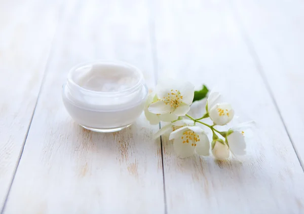 Pot of beauty cream surrounded by flowers on white wooden table — Stock Photo, Image