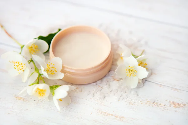 Ambiente de spa con flor de jazmín, olla de crema de belleza y sal marina sobre mesa de madera blanca —  Fotos de Stock