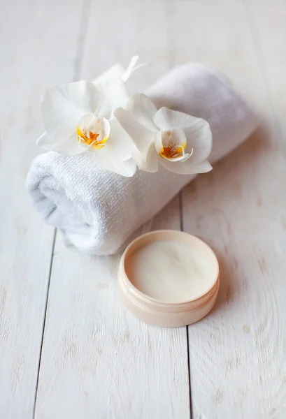 Crema facial con orquídea blanca y toalla sobre mesa de madera blanca . —  Fotos de Stock