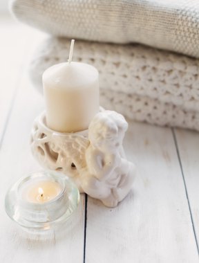 Beyaz ahşap masa üzerinde rahat örme kazak ve yanan mum yığını.