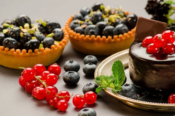 Tortas com mirtilos, groselhas vermelhas e chocolate na mesa — Fotografia de Stock