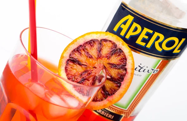 Glass of light drink and ice cube with bottle of Aperol