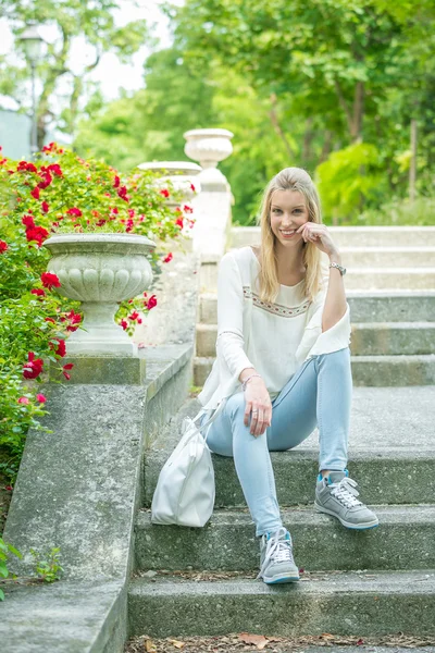 Porträtt av vacker flicka i parken sitter på trappsteget och uttrycker positivitet. — Stockfoto