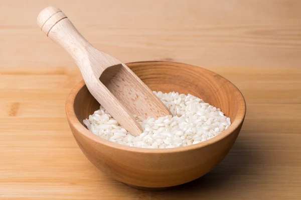Uncooked rice in wooden bowl with spoon on a wooden surface — Stock Photo, Image