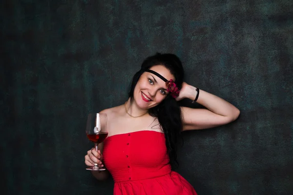 Hermosa mujer morena en vestido rojo con una copa de vino tinto — Foto de Stock