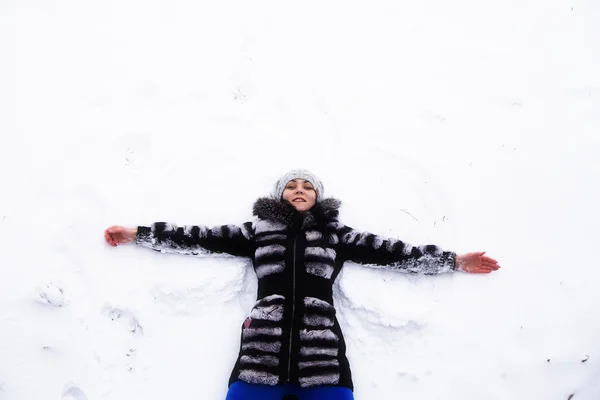 Glückliche junge Frau liegt im Winter auf Schneefell — Stockfoto