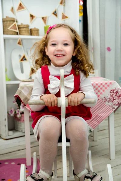 Pequena menina sorridente adorável no cavalo de brinquedo de madeira no interi — Fotografia de Stock