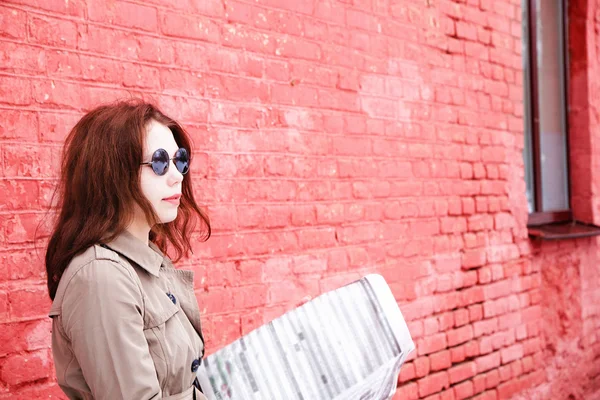 Attraktives junges Mädchen liest Zeitung über einer Ziegelmauer — Stockfoto