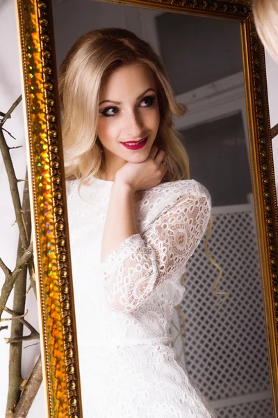 The beautiful girl in a long white dress looking into mirror. — Stock Photo, Image