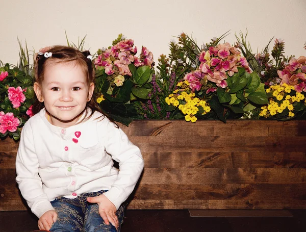 Petite fille heureuse sur une boîte en bois avec des fleurs — Photo
