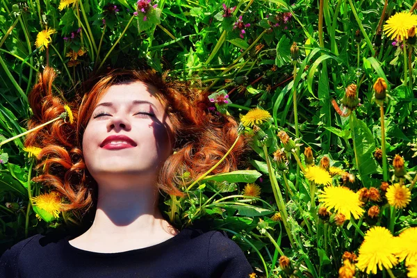 Girl with red hair lying on the field of dandelions — Stock Photo, Image