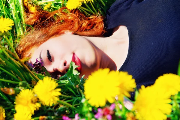 Девушка с рыжими волосами лежит на поле одуванчиков — стоковое фото