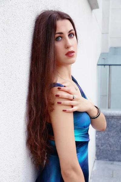 Schöne Mädchen in einem blauen Kleid vor einer weißen Wand — Stockfoto