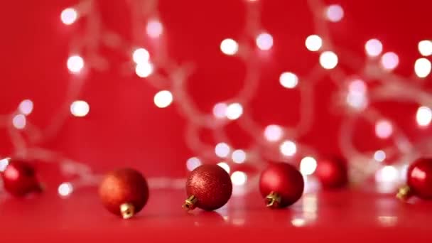 Rote Weihnachtskugeln rollen auf rotem Hintergrund. Weihnachtsgirlanden funkeln im Hintergrund — Stockvideo