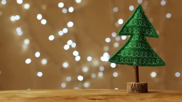 Albero di Natale giocattolo fatto a mano si erge su uno sfondo beige e una ghirlanda di Natale lampeggiante sullo sfondo — Video Stock