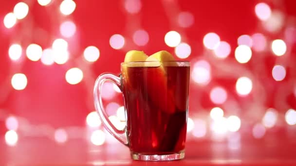 Una copa de vino caliente elaborado con vino tinto se alza sobre un fondo de guirnaldas rojas y espumosas — Vídeos de Stock